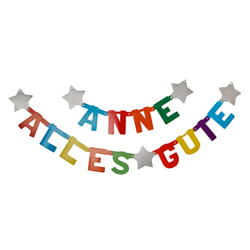Zwei PAPSTAR individualisierbare Grußketten der PAPSTAR GmbH hängen als fröhliche Dekoration: Auf der oberen steht "ANNE", auf der unteren "ALLES GUTE". Beide sind mit bunten, individualisierbaren Papierbuchstaben und weißen Sternen versehen. 1 Set in Faltschachtel.