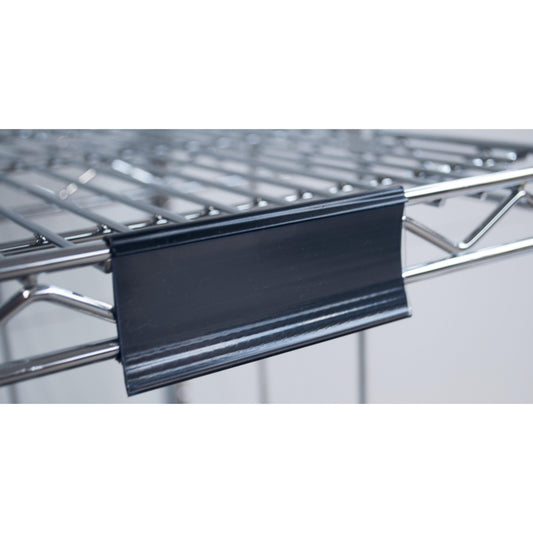 Nahaufnahme eines Novocal Etikettenrahmens mit Papierschildern (ca. 100 x 44 mm, 1 Stück), der an einem Metalldrahtregal befestigt ist, mit dem schwarzen Kunststoffetikettenhalter an der Vorderkante; der Hintergrund ist unscharf.