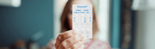 Person hält einen fluorecare Antigen Schnelltest mit Anzeige für COVID-19, Flu A/B und RSV vor unscharfem Hintergrund