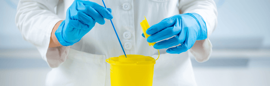 Person mit blauen Handschuhen entsorgt einen Tupfer in einem gelben Abwurfbehälter, Nahaufnahme in medizinischer Umgebung