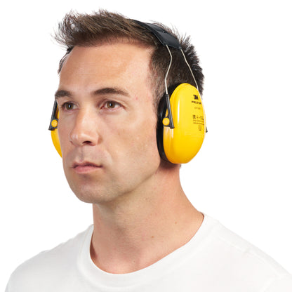 A man with short brown hair wears a bright yellow 3M™ PELTOR™ Optime™ I Ear Muffs H510A (SNR 27 dB) from 3M Deutschland GmbH and a simple white shirt. He looks straight ahead against a plain white background.