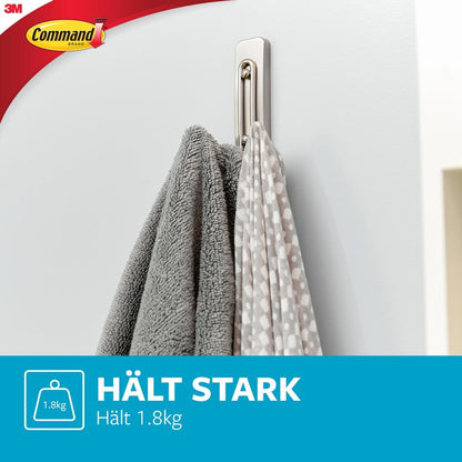 A Command™ Large Bathroom Double Hook Satin Nickel by 3M Deutschland GmbH is mounted on a white wall and holds a gray towel as well as a white one with gray dots. Text: "HOLDS STRONGLY Holds 1.8kg", with the 3M logo in the corner.