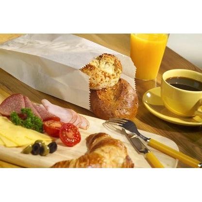 A breakfast spread with cheese, salami, ham, olives, and tomatoes on a board, a croissant, coffee, orange juice, and two rolls in PAPSTAR 1000 paper folding bags made of cellulose from PAPSTAR GmbH on a wooden table.