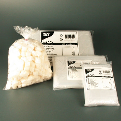 A transparent plastic bag with white sugar cubes lies next to three stacks of Starpak 500 flat bags, transparent LDPE, each in branded packaging with product information and the number 500, highlighting this high-quality packaging solution.