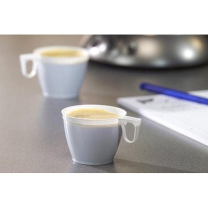 Two small Starpak coffee cups (PS, 0.18l, Ø7.8cm, white) from a set of 10 are filled with coffee on a gray surface, with a blue pen and a blurred white sheet of paper visible in the background.