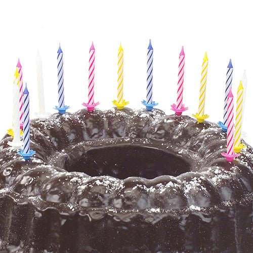 A chocolate cake sprinkled with powdered sugar and decorated with ten PAPSTAR birthday candles 6 cm, color assorted with holder (from PAPSTAR GmbH) in various colors.