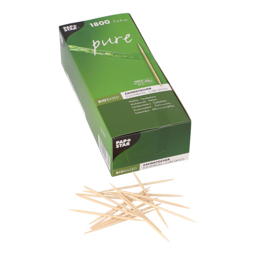 A green box from PAPSTAR GmbH with the label "pure" contains 1,800 round wooden toothpicks (6.8 cm) in a cardboard tray, with several eco-friendly toothpicks scattered on a white surface in front.
