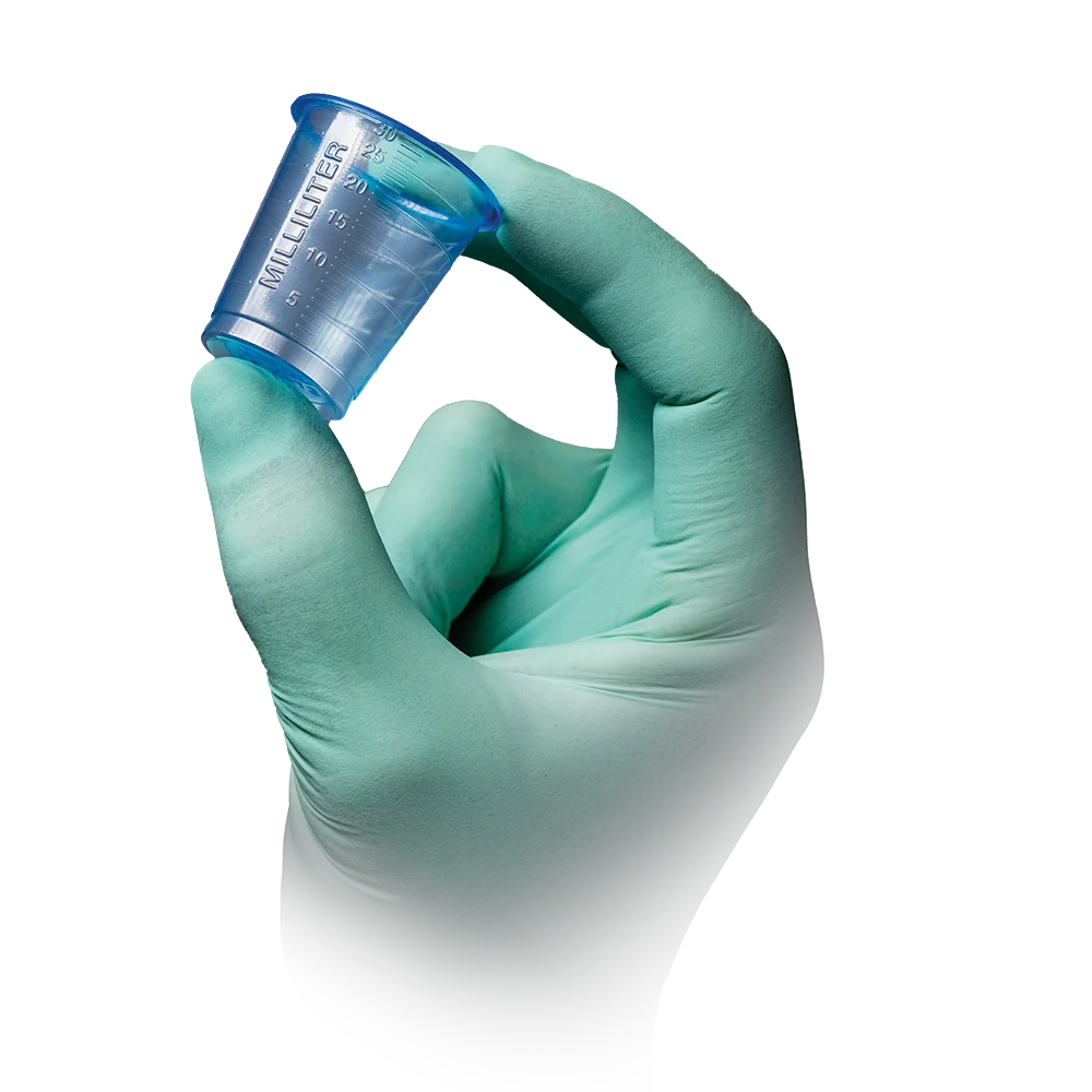 A light green gloved hand holds one of the AMPri PP medical cups 30 ml graduated in transparent blue by AMPri Handelsgesellschaft mbH with milliliter graduation on a white background.