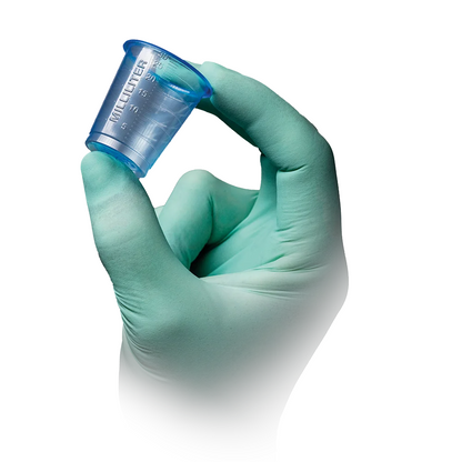 A light green gloved hand holds one of the AMPri PP medical cups 30 ml graduated in transparent blue by AMPri Handelsgesellschaft mbH with milliliter graduation on a white background.