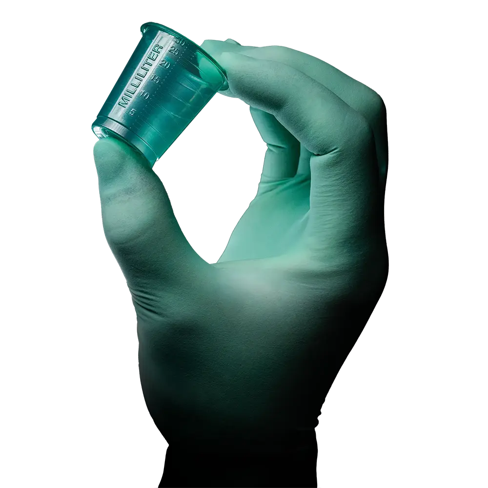A gloved hand holds a small, translucent green AMPri PP medical cup with embossed markings. The white background highlights the hand and the cup, which is manufactured by AMPri Handelsgesellschaft mbH from durable polypropylene.