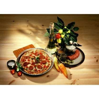 A pepperoni pizza lies on a plate next to white wine, sausage, and olives – freshly baked in Starpak 25 round molds aluminum round by Starpak for optimal heat conduction – accompanied by tomatoes, peppers, and a potted plant on a wooden table.
