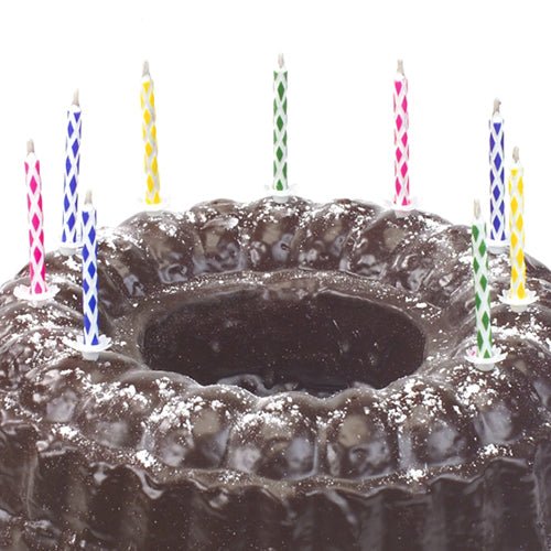 A chocolate cake sprinkled with powdered sugar is decorated with colorful PAPSTAR magic candles 6 cm (10 pieces per pack, with holder, from PAPSTAR GmbH) against a plain white background.