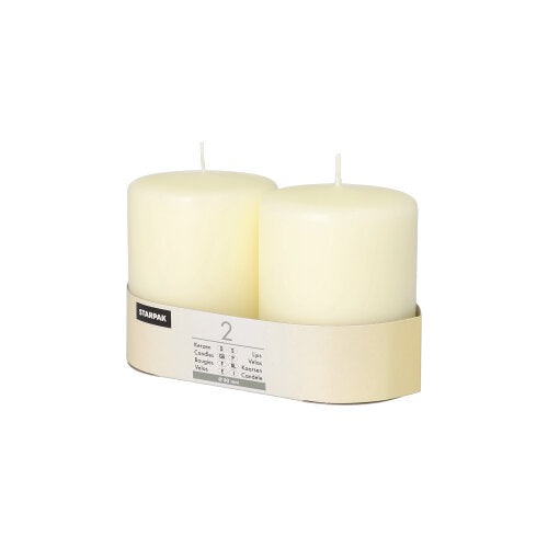 Two white Starpak 2 pillar candles Ø 80 mm with flat top stand side by side in a simple beige cardboard holder with a Starpak label and product details. The background is plain white.