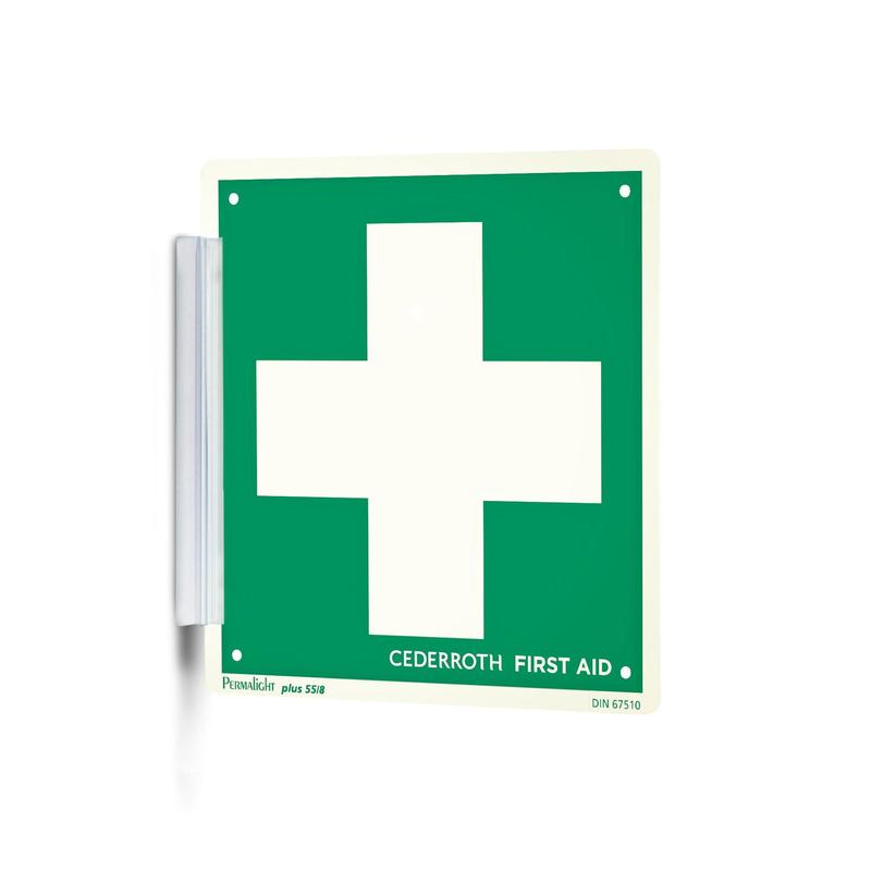 A green-white "Clip sign | Pack (1 piece)" from Orkla Wound Care AB with a large white cross and the inscription "Cederroth First Aid" is mounted on the wall like a signature stamp with a metal bracket and is thus clearly visible at the workplace.