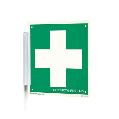 A green-white "Clip sign | Pack (1 piece)" from Orkla Wound Care AB with a large white cross and the inscription "Cederroth First Aid" is mounted on the wall like a signature stamp with a metal bracket and is thus clearly visible at the workplace.