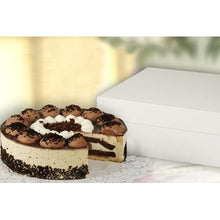 A round cake with layers of chocolate and cream sits on a lace doily next to a closed PAPSTAR 10 cake boxes with lids, white rectangular cardboard from PAPSTAR GmbH; a slice has been cut out, revealing the chocolate and cream inside.