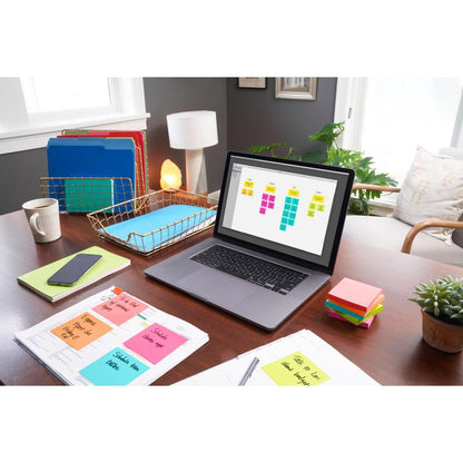 A home office desk with a laptop with digital sticky notes, colored folders, a smartphone, a lamp, papers with handwritten notes, a potted plant, and 3M Deutschland GmbH Post-it® Notes (76x127 mm, 100 sheets/block, 6 blocks/pack, 100% PEFC).