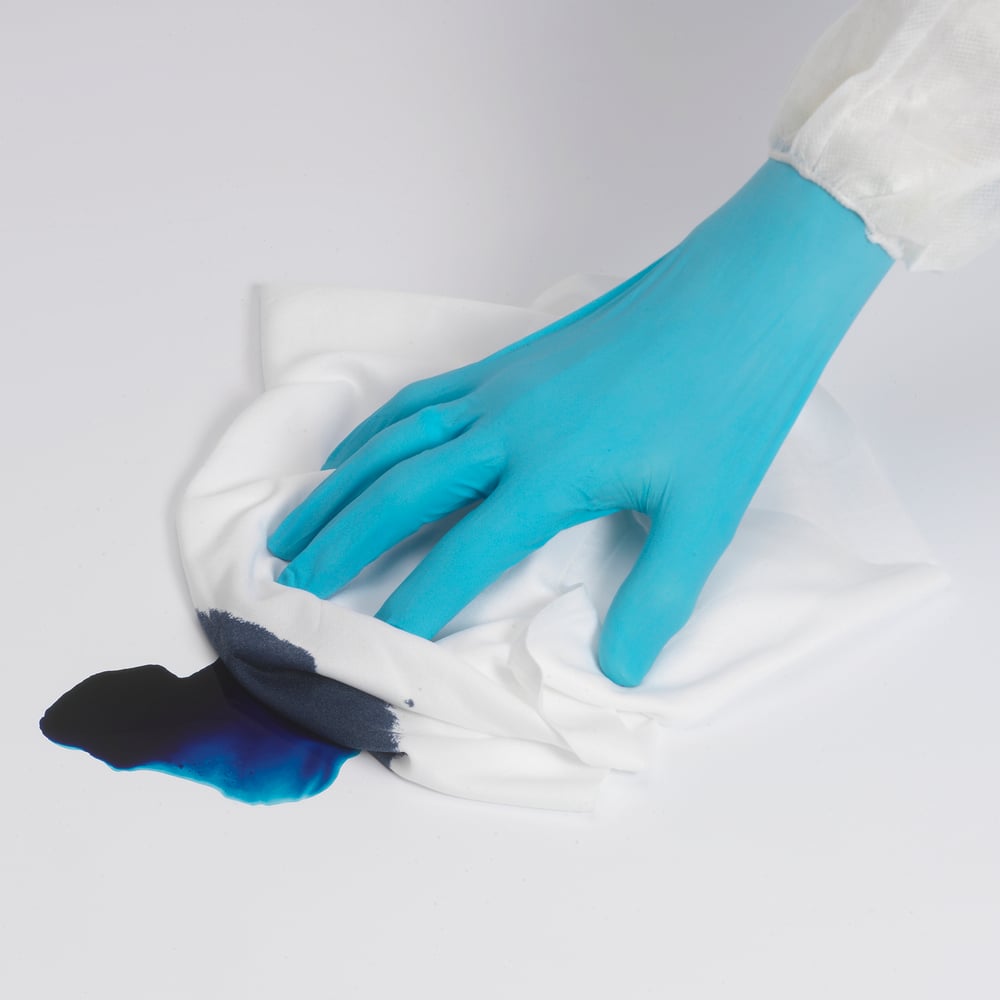 Eine Person mit einem blauen Handschuh wischt mit einem Kimtech® Polyester Flaschentuch (Weiß, Groß, 8x50 Blatt) der Kimberly-Clark GmbH eine dunkelblaue Flüssigkeit auf einer weißen Fläche auf.