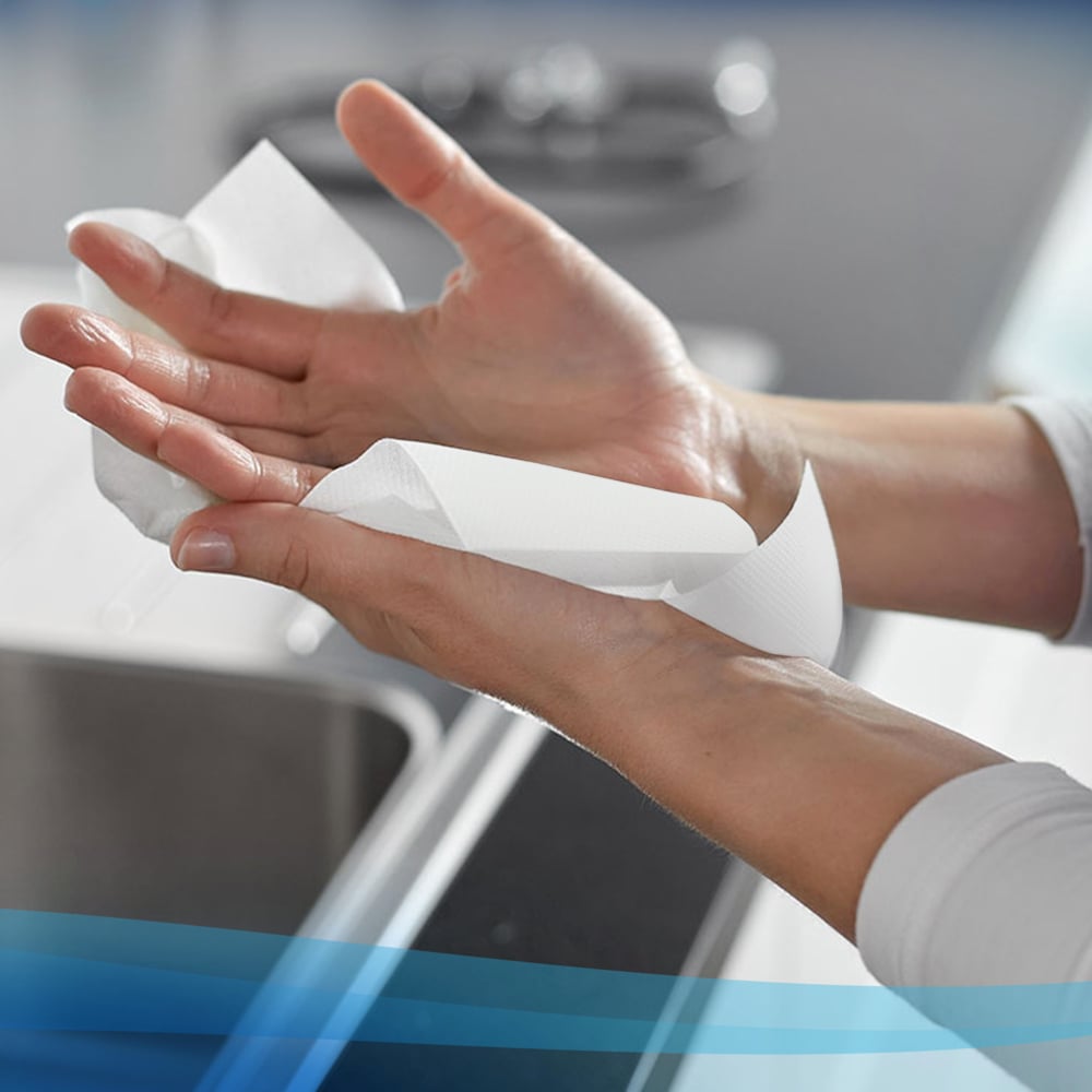 A person dries their hands with Scott® Control™ Slimroll™ paper towels from Kimberly-Clark GmbH over a kitchen sink, with a blurred countertop and faucet in the background for hygienic hand drying.