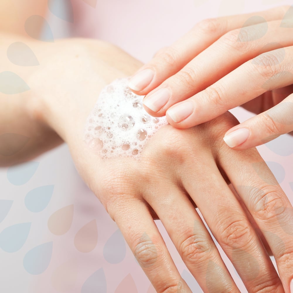 A person uses the Kleenex® Gentle Wash Lotion (1L cassette) from Kimberly-Clark GmbH for gentle hand cleaning and applies the foamy soap to the back of their hand against a bright background with a subtle water drop pattern.