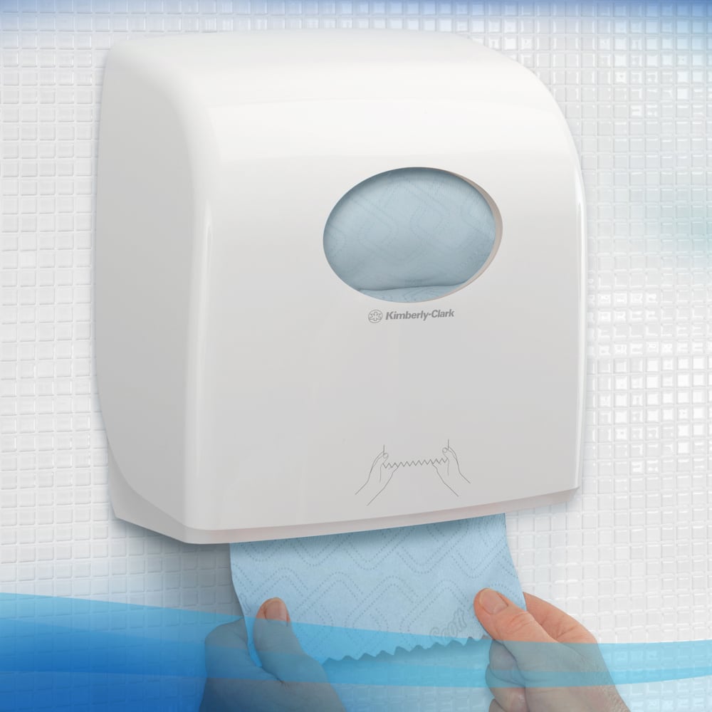 A white dispenser from Kimberly-Clark GmbH for Scott® Essential™ Slimroll™ Hand Towels (190.00 m x 19.80 cm) is wall-mounted, with a hand pulling out a blue towel, visible in the round window for environmentally friendly hand drying.