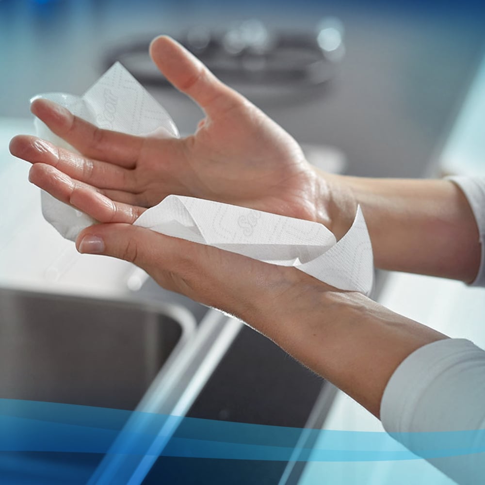 A person dries their hands with Scott® Essential™ Slimroll™ Hand Towels (190.00 m x 19.80 cm) from Kimberly-Clark GmbH using environmentally friendly hand drying in a modern kitchen near the sink.