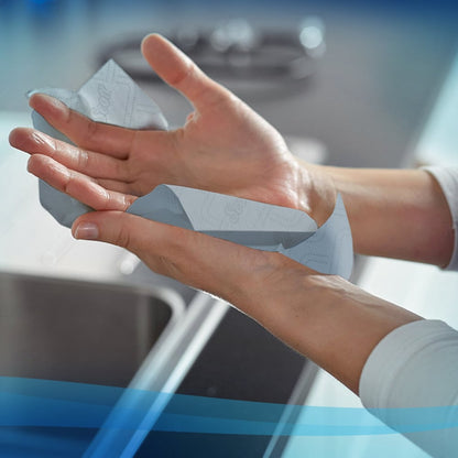 A person dries their hands with Scott® Essential™ Slimroll™ Hand Towels (190.00 m x 19.80 cm) from Kimberly-Clark GmbH over a sink in a modern kitchen - for environmentally friendly hand drying.