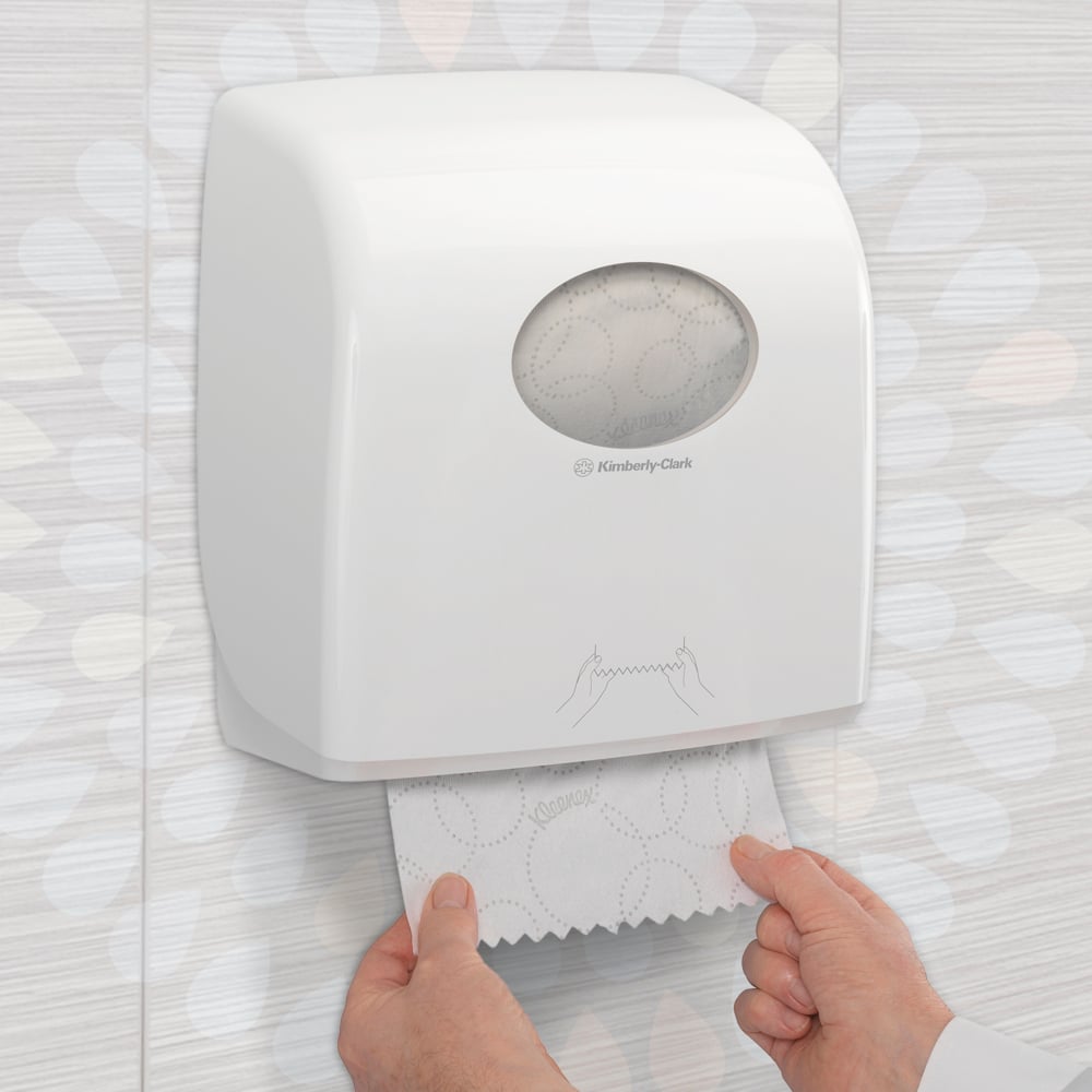 Jemand zieht ein Kleenex® Ultra™ Slimroll™ Handtuch aus einem weißen, an der Wand montierten Spender mit Sichtfenster und Symbolen in einer gefliesten Toilette. Produkt: 6-Rollen-Karton von Kimberly-Clark GmbH.