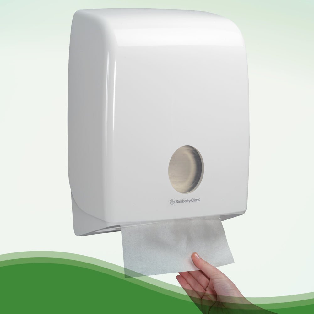 A hand pulls a Hostess™ NATURA™ white towel from Kimberly-Clark GmbH from a wall-mounted dispenser with a white plastic cover and viewing window - ideal for public restrooms. 20 clips x 84 sheets/carton.