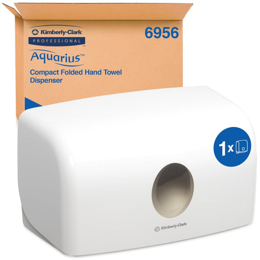 Ein weißer Aquarius™ Spender für gefaltete Handtücher von Kimberly-Clark GmbH (MultiFold, Klein) steht vor seiner braunen Verpackung. Der kompakte Behälter sorgt durch die runde Öffnung vorne für hygienische Papierentnahme.