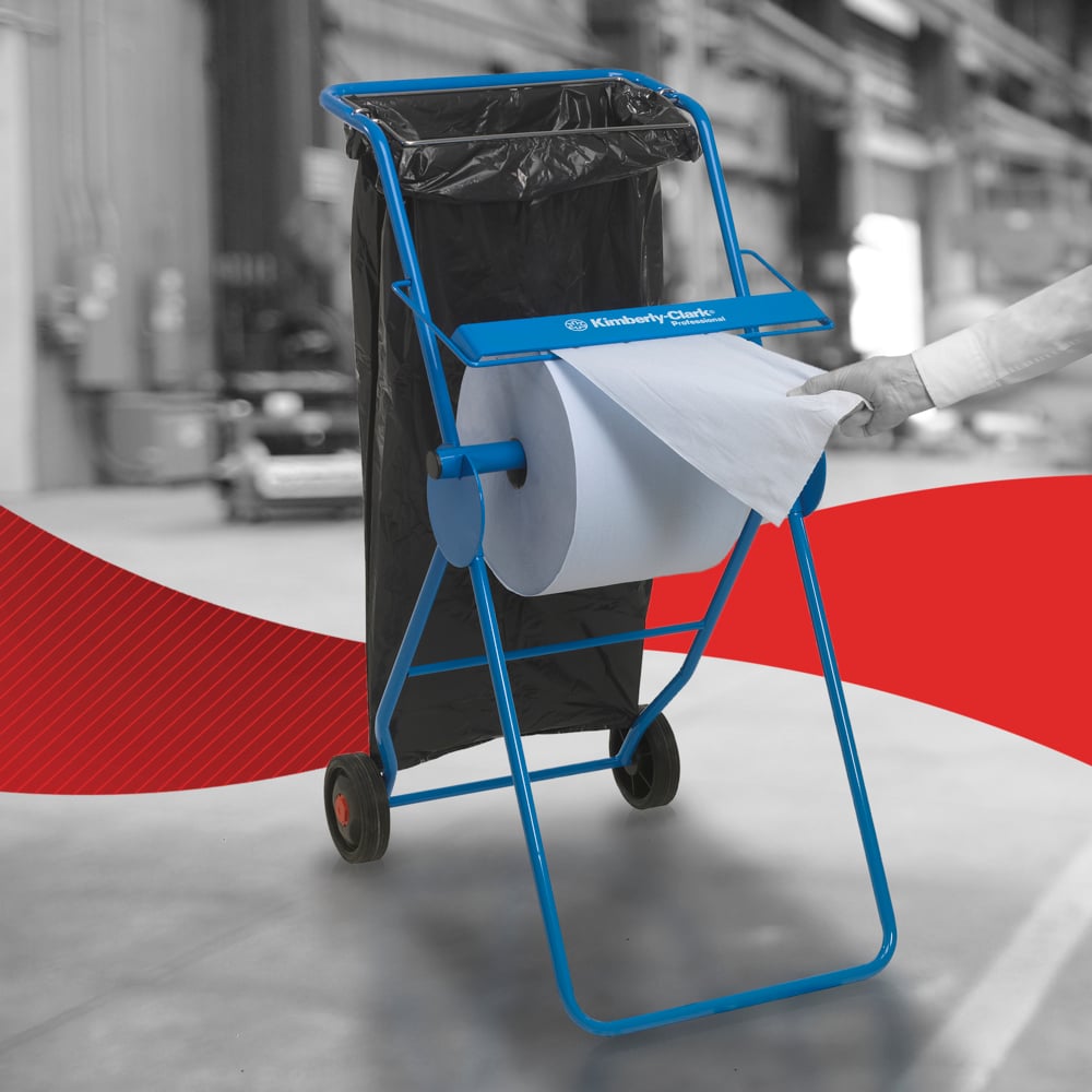 Eine Person zieht ein WypAll® L20 Papierwischtuch für Instandhaltungsarbeiten - Großrolle / Blau von Kimberly-Clark GmbH aus einem blauen Spender in einer Industrieumgebung, mit dem Kawasaki Robotics Logo und einem schwarzen Müllsack in der Nähe.