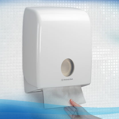 A hand pulls a Scott® Hand Towel - MultiFold / White from a wall-mounted dispenser by Kimberly-Clark GmbH in a tiled bathroom, ensuring hygienic hand drying.