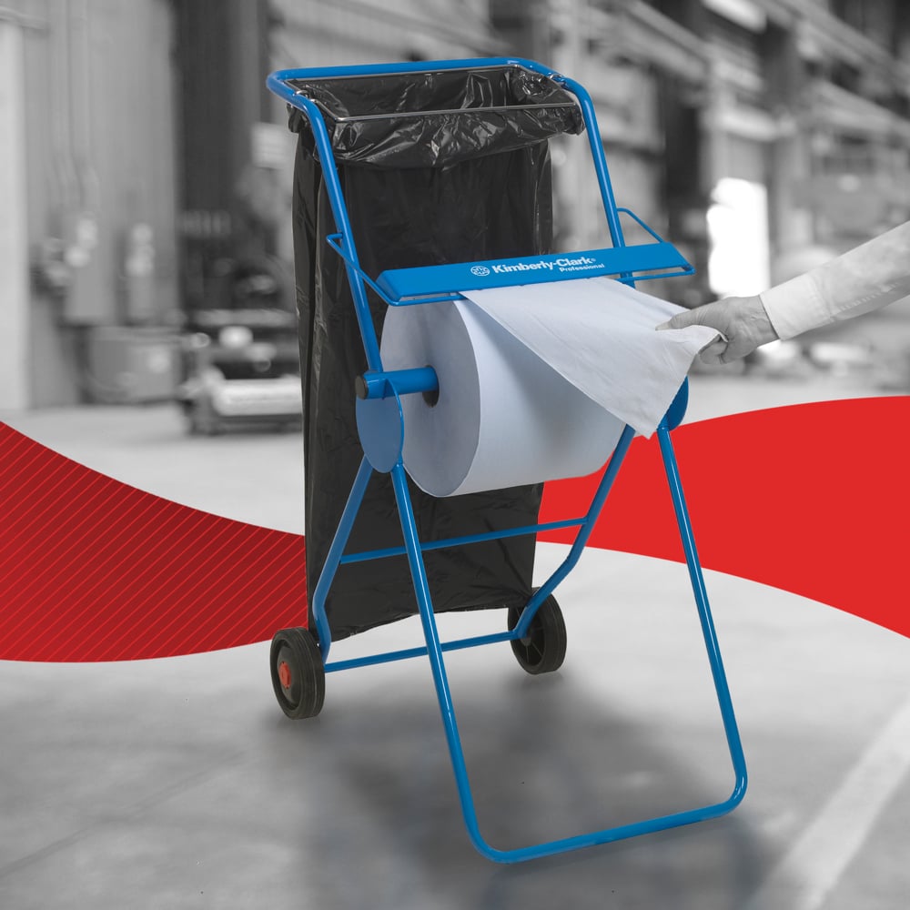 A person pulls a WypAll® L10 paper towel for surfaces - large roll (38.00 x 23.50 cm) from Kimberly-Clark GmbH from a blue metal stand with wheels and an attached black trash bag, indicating efficient surface cleaning in industrial environments.
