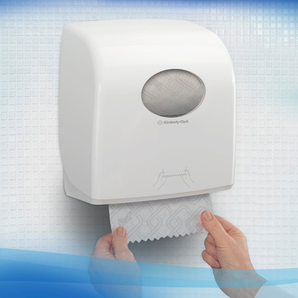 A person pulls Scott® CONTROL EXTRA STRONG towels from a wall-mounted, white dispenser by Kimberly-Clark GmbH, which is set against white, textured tiles. On the front of the roll towel dispenser, a simple usage instruction is displayed.
