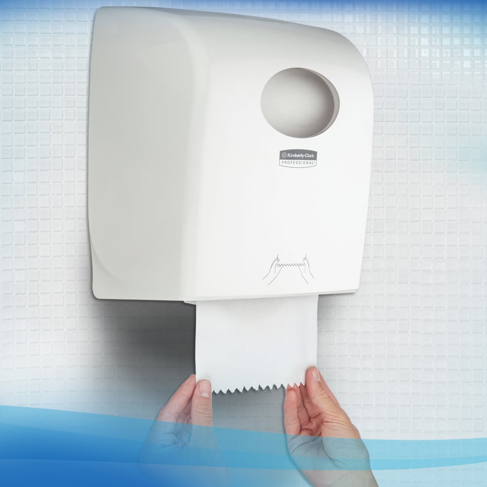 Eine Person zieht ein Scott® Control™ Handtuch - Rolle / Weiß aus einem weißen Wandspender der Kimberly-Clark GmbH in einer Toilette mit gefliesten Wänden und sorgt so für hygienisches Händetrocknen.