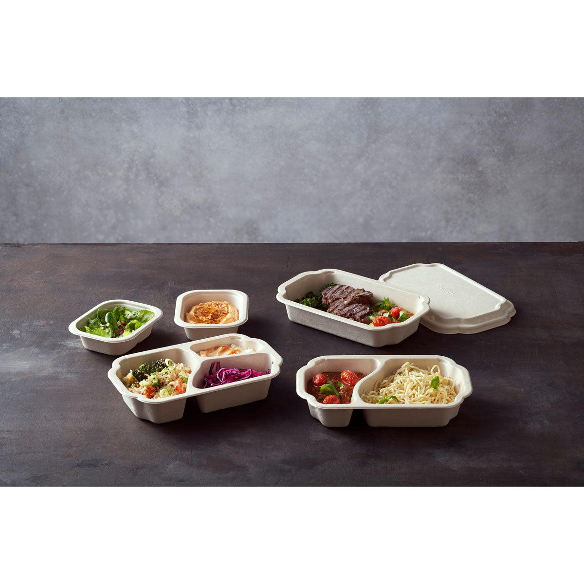 On a dark surface, there are several Tray Side Dish Fibre 1-Comp 55 mm Natural Coated Bagasse containers from Duni GmbH, each containing different dishes; a pack of 320 pieces includes a container with a partially opened lid.