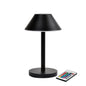 The LED lamp Zelda Midi by Duni GmbH in a modern graphite design with a round base and conical shade stands next to a remote control with colorful buttons - the ideal, energy-efficient lighting solution.