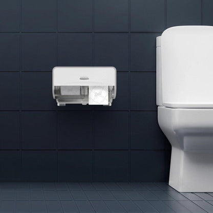 A wall-mounted dispenser holds two rolls of Scott® Essential™ Toilet Paper 8517 2-ply from Kimberly-Clark GmbH and is installed on a dark tiled wall next to a white toilet with a closed lid; the floor is also tiled in dark to match.
