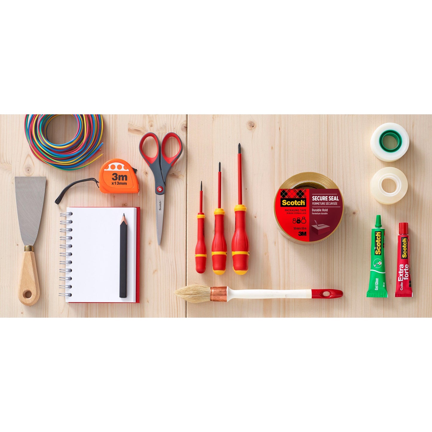 Eine Rolle Scotch® Verpackungsklebeband (50 mm x 66 m) der 3M Deutschland GmbH liegt übersichtlich zwischen Handwerkzeugen und Vorräten auf einer Holzfläche.