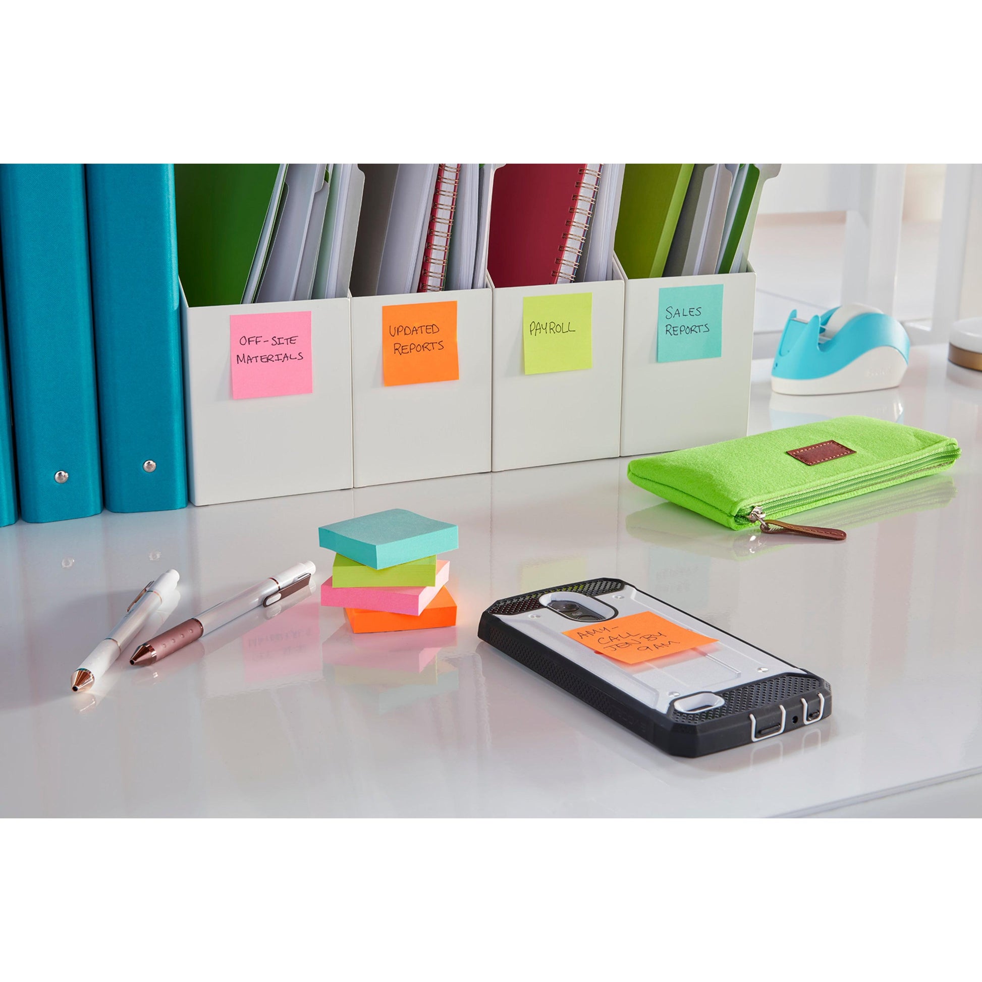 Ein aufgeräumter Schreibtisch mit grünem Federmäppchen, Stiften, 3M Post-it® Super Sticky Notes (47,6 x 47,6 mm, 90 Blatt, 100 % PEFC), einem Smartphone mit einer beschrifteten Notiz, Ordnern für Büromaterial und Berichte sowie einem blauen Klebebandabroller im Hintergrund.