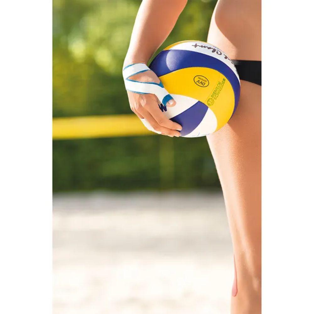A person in black swimwear stands on a sandy volleyball court with a blue-yellow-white volleyball. The visible lower body and thighs show no Leukotape Sport Tape Classic (BSN Medical GmbH) or signs of sports injuries.