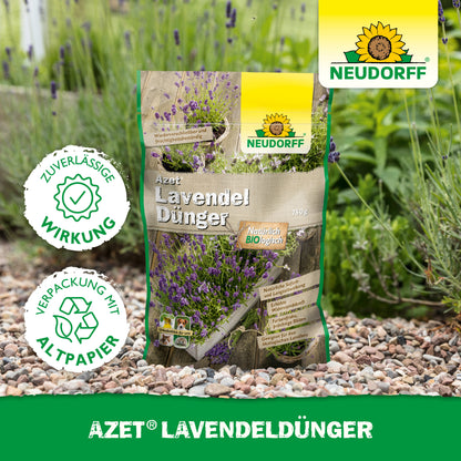 Eine Tüte Neudorff Shop Azet LavendelDünger liegt auf einem Gartenweg aus Kies neben Lavendel mit blau-violetten Blüten. Auf der Verpackung steht "umweltfreundlich" in deutscher Sprache.