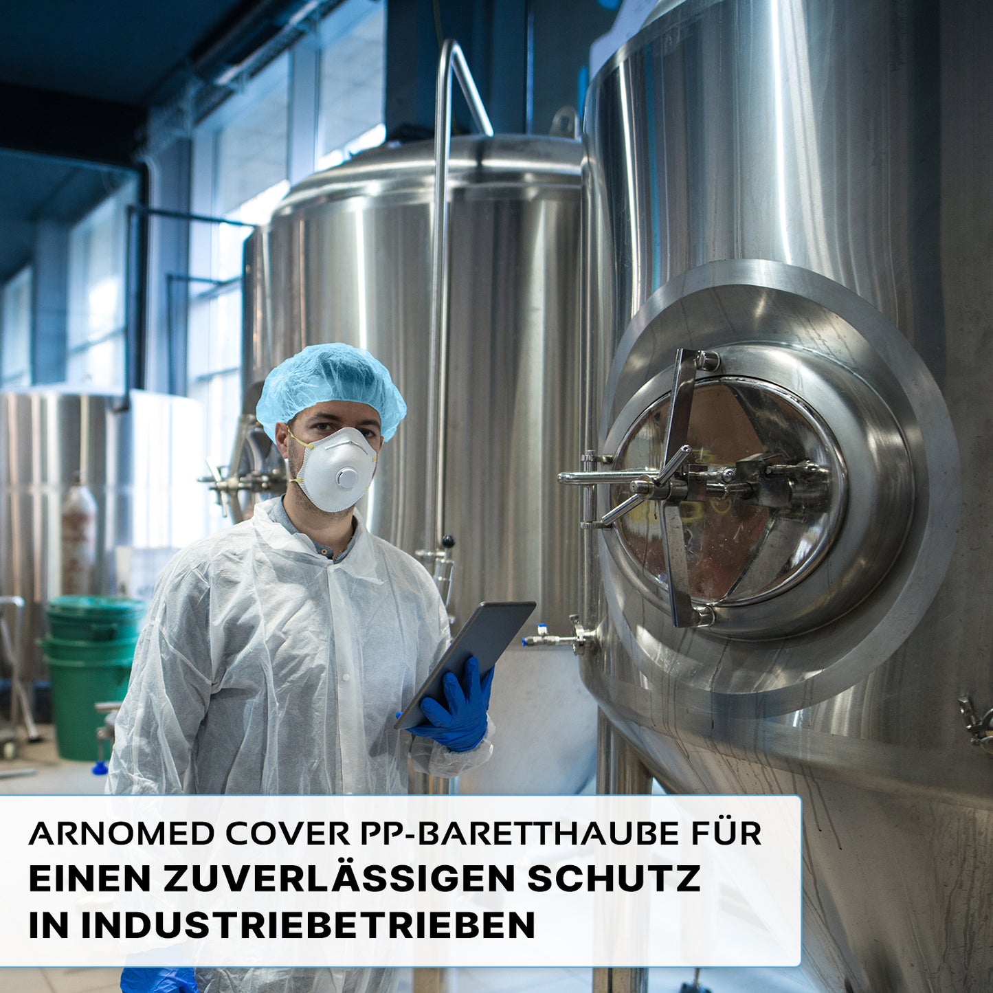 Eine Person, die eine ARNOMED COVER PP-BARETTHAUBE Baretthaube aus PP-Vlies der ARNOWA GmbH und eine Maske trägt, steht vor Edelstahltanks in einem industriellen Hygienebereich und hält ein Tablet in der Hand. Der deutsche Text hebt den zuverlässigen Schutz für die Industrie hervor.