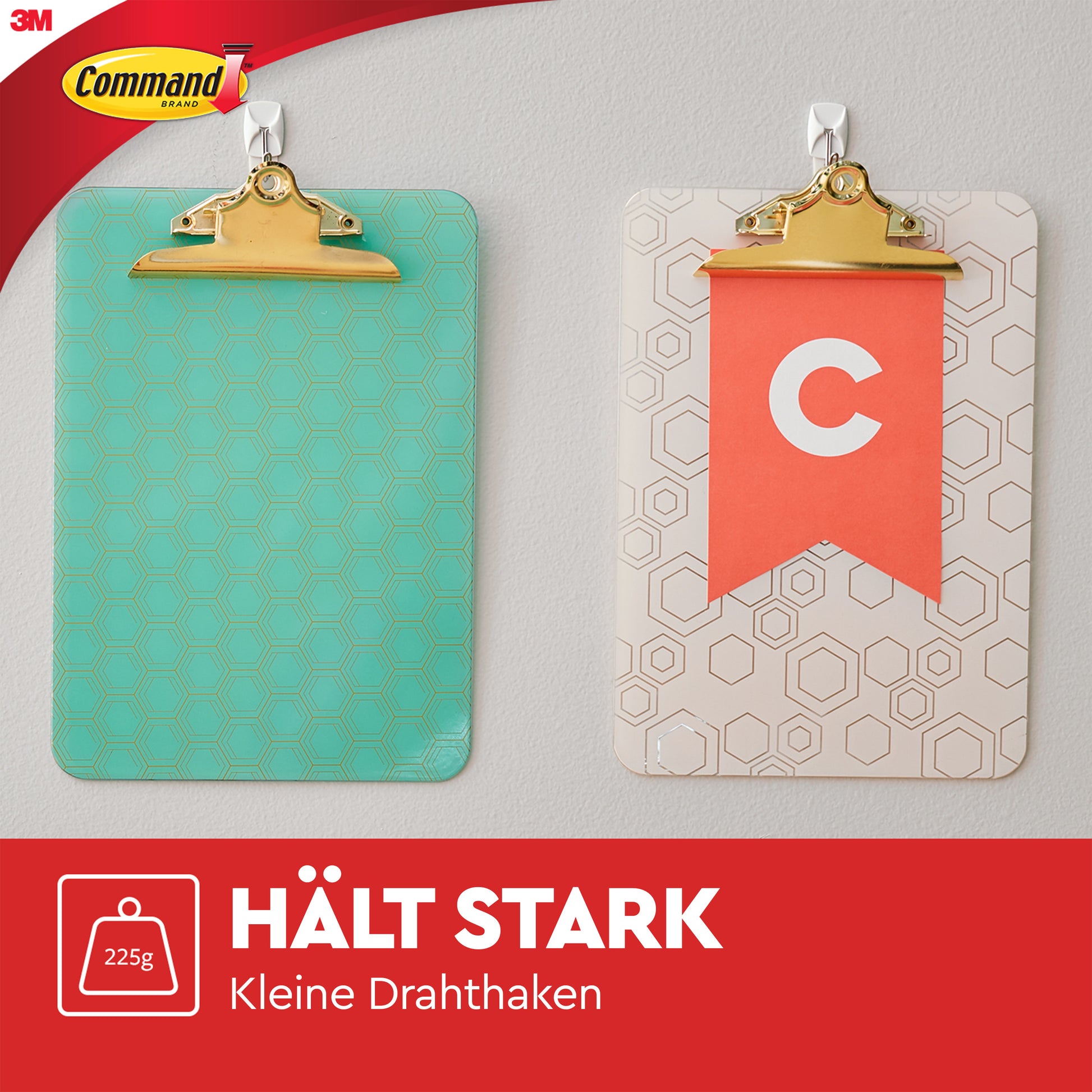 An der Wand hängen zwei Klemmbretter mit Command™ Small Drahthaken, 17067 von 3M Deutschland GmbH. Das linke Klemmbrett ist tealfarben mit Sechsecken, das rechte zeigt ein rotes Banner und ein weißes "C". Das 3M-Logo ist ebenfalls zu sehen.
