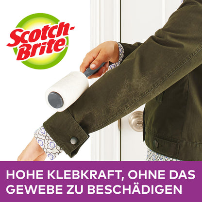 Eine Person verwendet die Scotch-Brite™ Everyday Clean Ersatz-Fusselrolle (30 Blatt, 1 Stück) von 3M Deutschland GmbH auf dem Ärmel einer dunkelgrünen Jacke. Unten steht: "Hohe Klebkraft, ohne das Gewebe zu beschädigen.