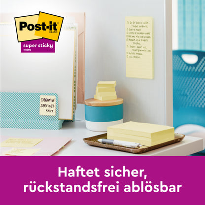On a tidy desk, 3M Deutschland GmbH Post-it® Super Sticky Notes Cube, Yellow, 76 mm x 76 mm, are stacked with folders and pens. A note sticks securely and leaves no residue. The German text emphasizes the strong hold.