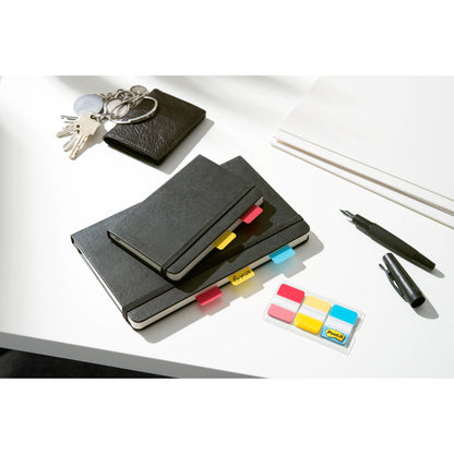 A set of black notebooks with Post-it® Index Strong Filing Tabs from 3M Deutschland GmbH in various colors, a wallet, keys, white paper, a black pen, and a marker lie on a white desk.