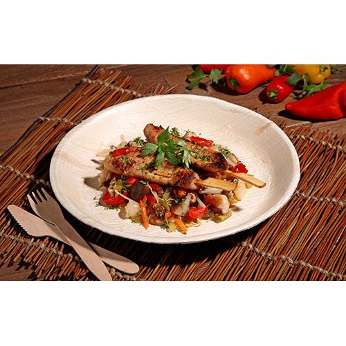 Grilled meat skewer with mixed vegetables and herbs is served on a PAPSTAR 25 plate, palm leaf "pure" round from PAPSTAR GmbH, with environmentally friendly disposable tableware and colorful bell peppers and vegetables in the background.