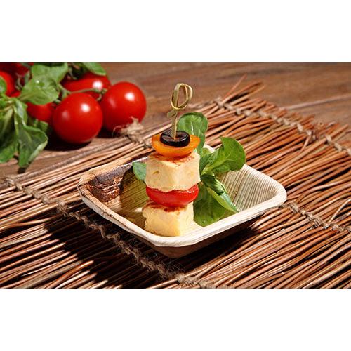 A skewered appetizer lies on a PAPSTAR 25 bowl, palm leaf "pure" round bowl from PAPSTAR GmbH, with fresh cherry tomatoes and vegetables on a woven mat - perfect for sustainable events.