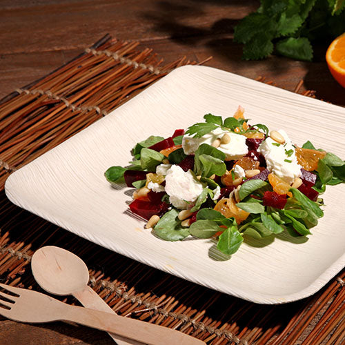 A stylish PAPSTAR 25 plate, palm leaf "pure" from PAPSTAR GmbH, serves a fresh salad on a woven placemat – ideal for special occasions with its eco-friendly design.